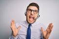 Young call center operator business man with blue eyes wearing glasses and headset crazy and mad shouting and yelling with Royalty Free Stock Photo