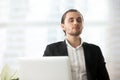 Young calm businessman resting at workplace with eyes closed.