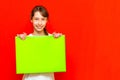 Young calm caucasian teenager girl holding blank paper sheet over red wall