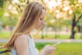 Young calm girl using her mobile phone to send a text while standing in a park Royalty Free Stock Photo