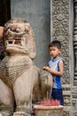 Young Cambodian boy waiting outside a temple with statue