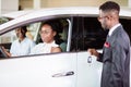 Sales situation in car dealership, young african couple gets the key for new car