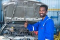 young car mechanic working by showing thumb up by looking at camera at garage - concept of approval, car repair service Royalty Free Stock Photo