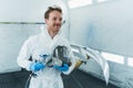 Young car paint service worker stands in a automobile painting booth with a gun and a protective mask in his hands. Royalty Free Stock Photo