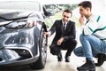 Young car salesman showing the advantages of the car to the customer and tires.