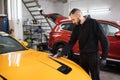 Young car wash worker wearing protective gloves, cleaning modern yellow car with microfiber cloth Royalty Free Stock Photo