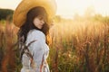 Young carefree female in rustic linen cloth relaxing in summer meadow. Stylish boho woman with straw hat posing among wild grasses Royalty Free Stock Photo