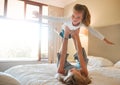 Young carefree mother holding up her daughter pretending to fly playing on a bed at home. Happy playful little girl Royalty Free Stock Photo