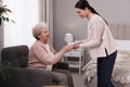 Young caregiver giving tea to senior woman. Home care service Royalty Free Stock Photo