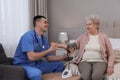 Young caregiver measuring blood pressure of senior woman in bedroom. Home health care service Royalty Free Stock Photo