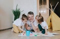 A young caring father learns to paint with his young daughters, a man lies on the floor and teaches girls to draw flowers, home