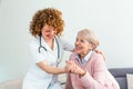 Young caring lovely caregiver and happy ward. Image of caregiver and senior resting in the living room. Smiling caregiver taking