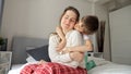 Young caring and loving boy hugging his upset mother sitting on bed. Concept of loving family, parents and kids, love and support Royalty Free Stock Photo