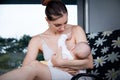 Young caring mother breastfeeding her little baby on grey house background