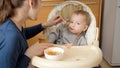 Young caring mother giving porridge to her baby son with spoon