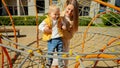 Young caring mother helping her baby son climbing up on the rope net at playground. Children playing outdoor, kids outside, summer Royalty Free Stock Photo