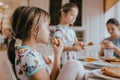 Young caring mother and her two little daughters eating pancakes with honey at the breakfast in the cozy kitchen