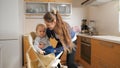 Young caring mother seating her baby in highchair on kitchen before giving breakfast. Concept of parenting, healthy nutrition and