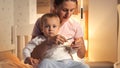 Young caring mother sitting with her baby boy in children's room and cutting his nails with scissors. Parenting, chil