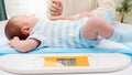 Young caring mother stroking her little newborn baby son while weighing him on digital scales in hospital. Concept of Royalty Free Stock Photo