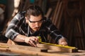 Young carpenter caucasian man using measuring tape looking wood size at workspace. craftsman profession in wood factory