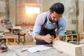 Young carpenter caucasian man using measuring tape looking wood size at workspace. craftsman profession in wood factory