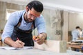 young carpenter caucasian man using measuring tape take note wood size at workspace. craftsman profession in wood factory Royalty Free Stock Photo