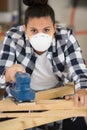young carpenter wearing filter mask sanding wooden work piece