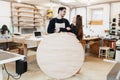 Young carpenter in carpenter workshop. The man holds a wooden round board for the text. Copyspace. young specialist, startup