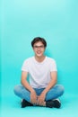 Young casual asian man sitting on the floor with his legs crossed and smiling for the camera. on blue background Royalty Free Stock Photo