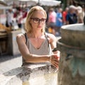 Young casual cucasian woman washing hands with water from public city fountain on a hot summer day