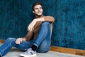 Young casual fashion man sitting on the floor  on dark blue background. Royalty Free Stock Photo