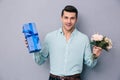 Young casual man holding gift box and flowers Royalty Free Stock Photo