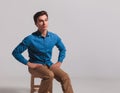 Young casual man sitting on chair with hands on waist Royalty Free Stock Photo