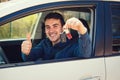 Young casual man wearing blue shirt holding car keys out of the window, showing thumb up positive gesture Royalty Free Stock Photo