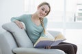 Young casual woman reading a book while sitting smiling on couch Royalty Free Stock Photo