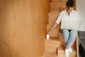 Young casual woman shopping online or working online from home and smiling. Happy stylish girl using laptop, sitting on wooden Royalty Free Stock Photo