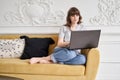 Young casual woman using black laptop while sitting on sofa in living room at home. Beautiful cheerful girl using laptop Royalty Free Stock Photo