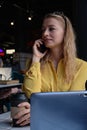 young cauasian pretty woman at coffee shop with laptop, calling by smartphone