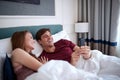Young caucasian adult couple laying in bed watching content on cell phone, laughing