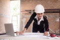 Young caucasian architect woman looking laptop and working drawing blueprint for planning building house on desk. Royalty Free Stock Photo