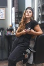 Young caucasian barber woman holding a straight razor and scissors standing at workplace