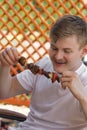 Young caucasian blond man have fun outdoors in summer weekend at barbeque grilling and eating meat skewers with friends. Royalty Free Stock Photo