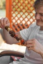 Young caucasian blond man have fun outdoors in summer weekend at barbeque grilling and eating meat skewers with friends. Royalty Free Stock Photo