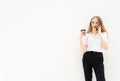 A young caucasian blonde business woman is standing in front of a white wall, talking to the phone, looking away, thinking and Royalty Free Stock Photo