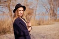 Young caucasian blonde girl in a dress, coat and hat in spring on beach, under rays of sun with willow branches, smiling Royalty Free Stock Photo