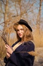 Young caucasian blonde girl in a dress, coat and hat in spring on beach, under rays of sun with willow branches, smiling Royalty Free Stock Photo