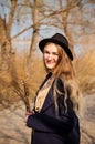 Young caucasian blonde girl in a dress, coat and hat in spring on beach, under rays of sun with willow branches, smiling Royalty Free Stock Photo