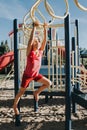 Young Caucasian blonde girl hanging on monkey bars in park on playground. Summer outdoors activity for kids. Active preschool