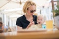 Young caucasian blonde mother spoon feeding her little infant baby boy child outdoors on restaurant or cafe terrace in Royalty Free Stock Photo